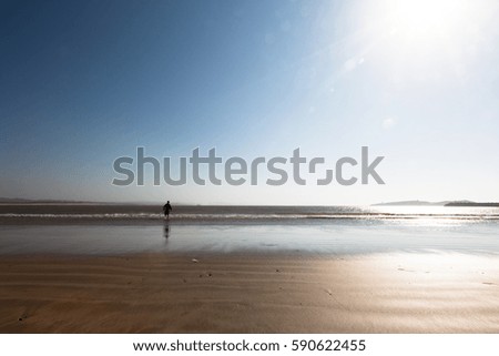 Young boy running on ocean beach wants to catch a ball from water. Light blue sky with bright sun in background