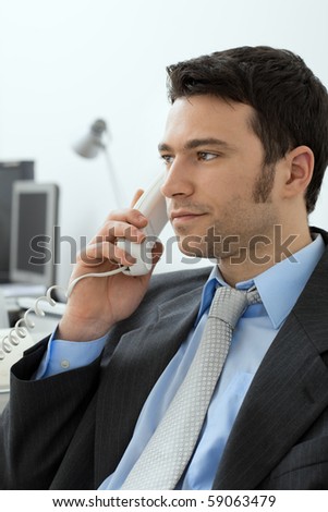 Closeup of businessman sitting at desk in office, talking on landline phone.
