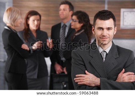 Portrait of young businessman wearing grey suit, standing with arms crossed in office.?