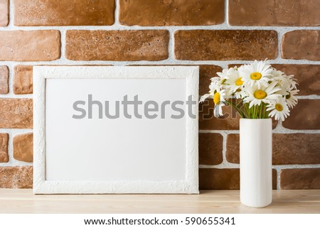 White landscape frame mockup with daisy bouquet flowers in in styled vase near exposed brick wall. Empty frame mock up for presentation design.  Template framing for modern art.