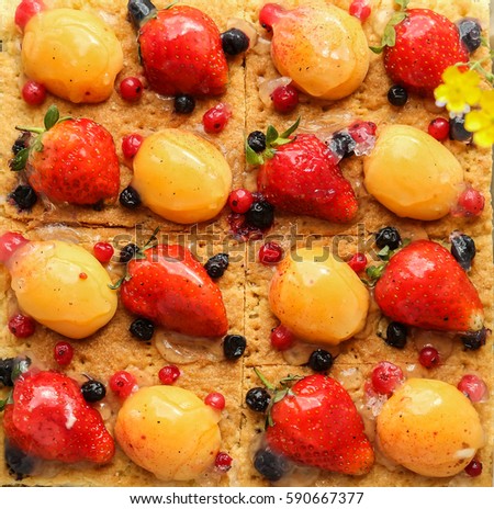 The pictures are very large cheesecake with berries, top view, vegetarian food , strawberry, and apricot, red and black currants, fruits are filled with agar-agar, side bouquets of wild flowers, cute
