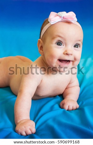 Cute smiling baby girl in a pink headband on a textile navy blue background