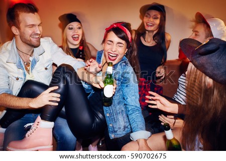 Group of trendy young people getting drunk at late night swag party, going crazy and laughing while sitting on sofa with beer bottles Royalty-Free Stock Photo #590702675