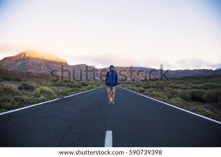 Portrait of man in blue jacket standing straight in the middle of road on mountains background, Tenerife Island
