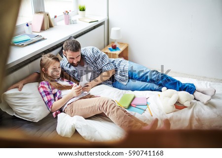 Pretty family of two lying on bed and playing games on digital tablet