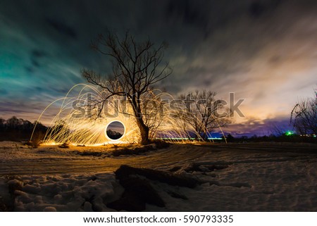 Abstract picture with trajectories of burning sparks near the tree at the background of spring night landscape