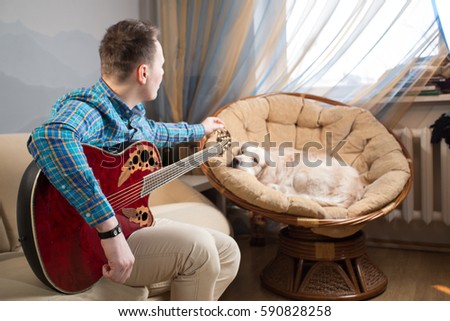 guy playing a guitar on the couch, in the chair sits a dog, a golden retriever