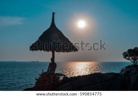 Beautiful landscape view of silhouette bamboo parasol and a man sit on the chair, in the evening with sunset, in small island, Thailand.