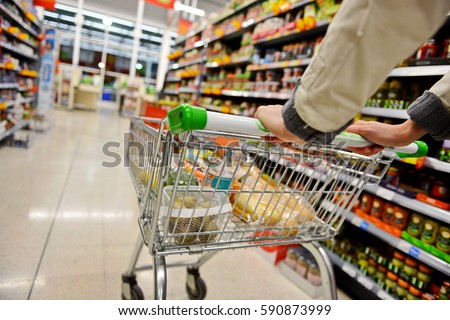 A Shopper Pushes a Trolley along a Supermarket Aisle - Image has a Shallow Depth of Field Royalty-Free Stock Photo #590873999