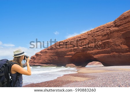 Tourist with backpack taking picture of rocks on Legzira beach, Morocco