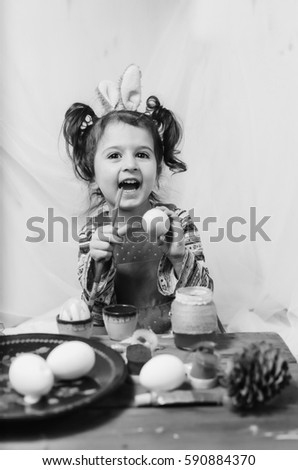 little girl 2 - 4 years in a red dress draws intently the pictures on the eggs with watercolors . at the head of the child ears of a rabbit preparing for Easter black and white , monochrome