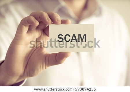 Closeup on businessman holding a card with text SCAM , business concept image with soft focus background and vintage tone