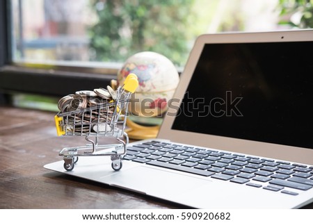 Small shopping cart filled with coins and miniature airplane on laptop using as business online concept.