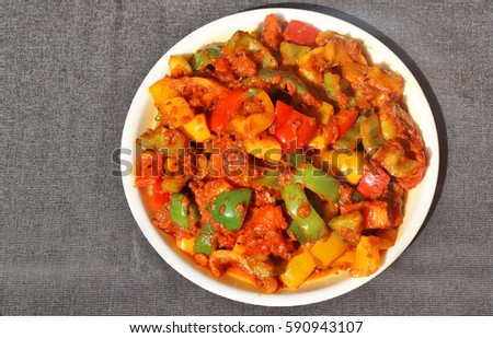 Indian style tricolour shimla mirch ki Sabzi (spicy capsicum vegetable) in white plate on black background.