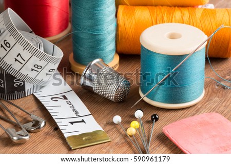 Spools of thread and basic sewing tools including pins, needle, a thimble, and tape measure on a wooden tabletop Royalty-Free Stock Photo #590961179