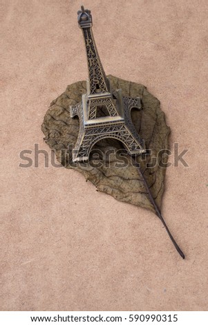 Little model Eiffel Tower  and a dry leaf on brown background