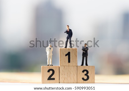 Miniature people: Small businessmen figures standing on wooden podium 1, 2, 3 with cityscape background Royalty-Free Stock Photo #590993051