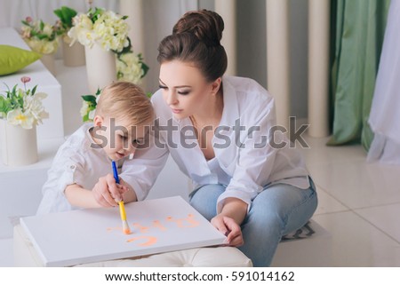 Mother and son play in a bright room. Mom draws a picture with your child. handsome boy with white hair and big eyes. Family in white of clothes. Communication with your child. Educational games.