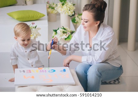 Mother and son play in a bright room. Mom draws a picture with your child. handsome boy with white hair and big eyes. Family in white of clothes. Communication with your child. Educational games.
