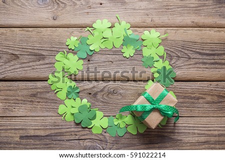 Round frame of clover leaves and gift box on the old wooden boards. St.Patrick's day background. Space for text, top view.