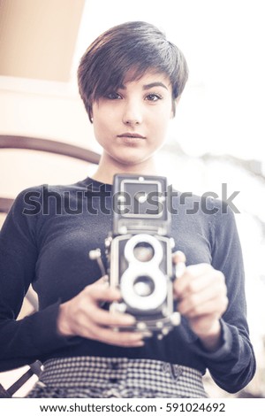 Young pretty woman posing and looking at camera with vintage bi optical camera between hands