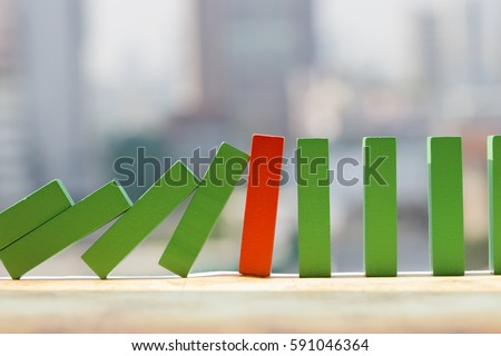 Leadership and risk management  concept. One red wooden domino stopping the effect of green wooden blocks with cityscape background