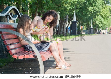 woman and her two young children watching a book on a bench in the park
