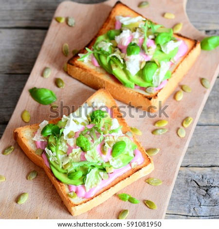 Open sandwiches with avocado, lettuce, basil, pumpkin seeds and creamy pink beet sauce. Simple and healthy vegan sandwiches on a wooden board. Closeup