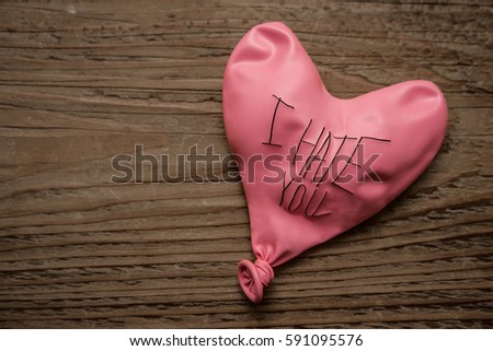 deflated pink red balloon with the words: i hate you lie on wooden table. 