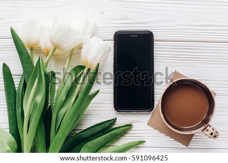 phone and tulips and morning coffee on white wooden rustic background. flat lay with flowers and gadget with empty screen with space for text. hello spring concept. good morning