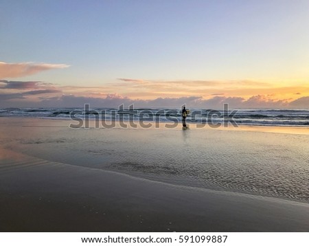 A lone surfer on the beach at sunrise