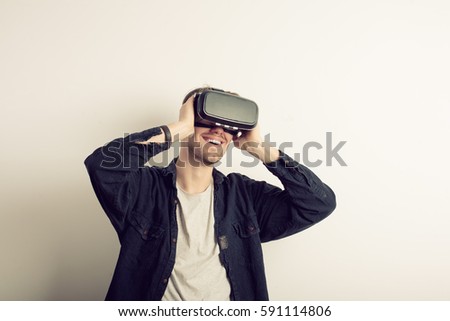 Young man wearing virtual reality headset or 3d glasses, standing against grey wall background