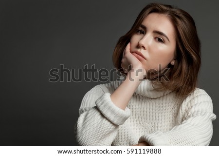 Serious pensive woman on gray background in a white sweater looking at the camera.