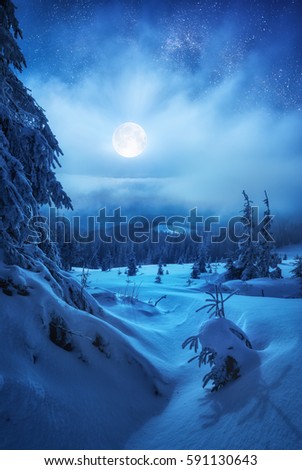 Raising of the full moon in a misty starry sky. Winter valley covered with snow.