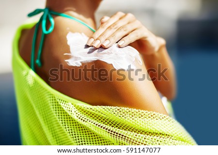 Woman applying sunscreen on her shoulder Royalty-Free Stock Photo #591147077