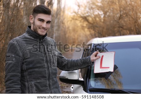 Young man removing label from car windscreen after getting driver's license