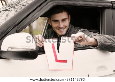 Young man tearing learner driver sign while looking out of car window