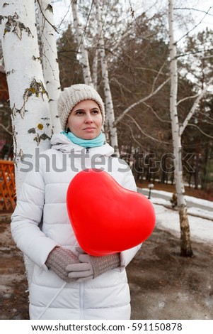 The woman in the middle of trees keeps in warm clothes naduveny the balloon in the form of heart
