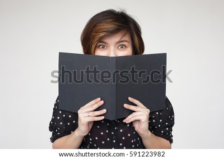 Asian girl covers her face with book, looking forward to the surprise. She is shocked with  information