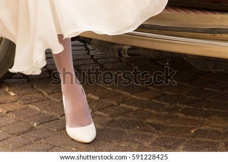 woman dressed in white chiffon dress, white shoes and panty hose stepping out of a car onto cobblestone pavement