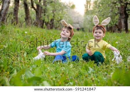 Catholic Easter tradition egg hunt. Two brother sibling boy kids dressed in bunny ears in spring garden with baskets searching eggs. Kids happy and smiling looking to each other celebration holiday