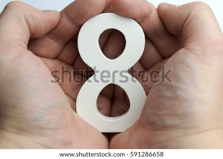 Hand holding number eight on white background.