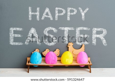 Happy Easter chalk sign on the grey surface, painted eggs in a cute wooden holder, close-up. Light table. Easter greetings.