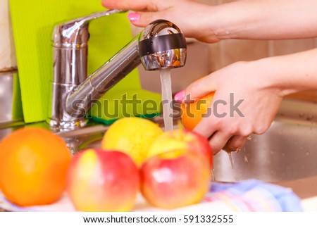 Woman young housewife washing fresh apple orange fruits in kitchen under water stream, preparation salad vegetarian meal. Healthy eating, cooking, dieting and people concept