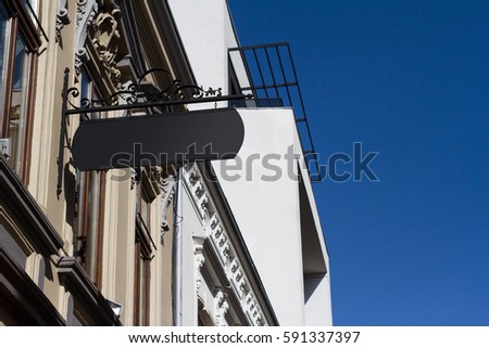 Horizontal front view of empty black square vintage signage on a white building with classical architecture hanging with chains