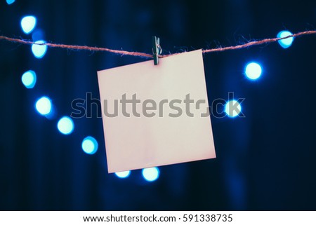 Blank square. One note paper on christmas bokeh background. paper notes hanging on rope with clothespins, copy space for your text or image or product placement.