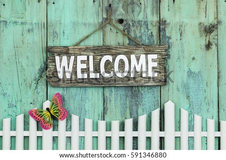 Wood WELCOME sign hanging by rope over white picket fence with colorful spring butterfly and rustic antique mint green background; springtime and home decor background with painted wooden copy space