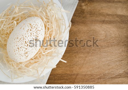 Table Setting for Easter Celebration. Carved Egg in the Nest on Wooden Background. Holidays background. Spring Time. Selective Focus. Copy Space.
