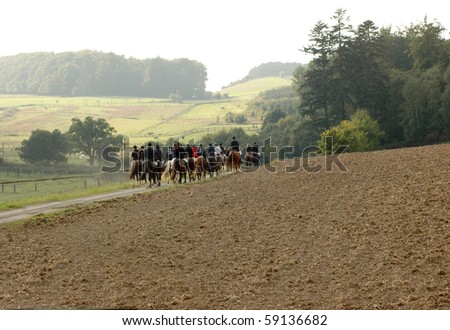 The group of equestrians ride through the field.