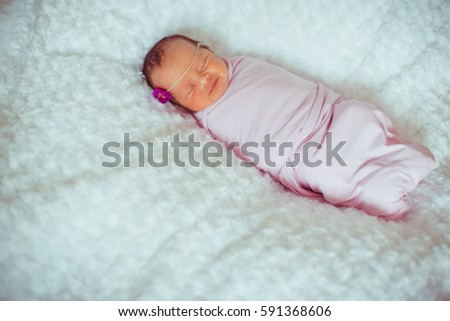 Newborn baby-girl with violet flower on her head lies on fluffy blanket